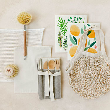 A top-down view of many waste-free products, including bags, a set of utensils, and some cleaning products, sit on a light tan background.