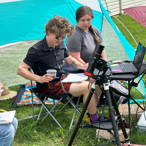 Students Max and Quincy seated looking through telescopes