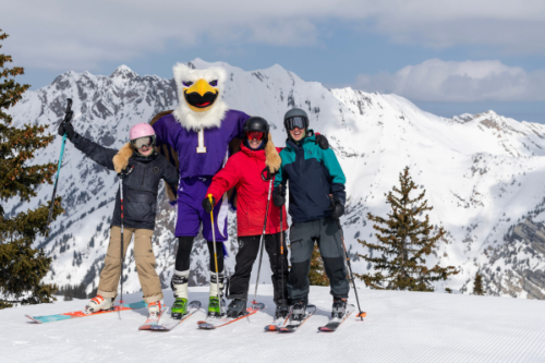 Westminster mascot Griff poses with three skiers in colorful jackets on a ski slope.