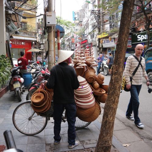 a hat vendor on a street in Vietnam with a white male walking by