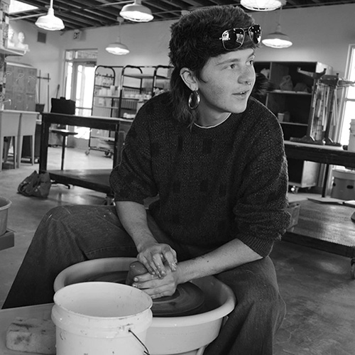 Brittyn working at a pottery wheel, looking off to the side