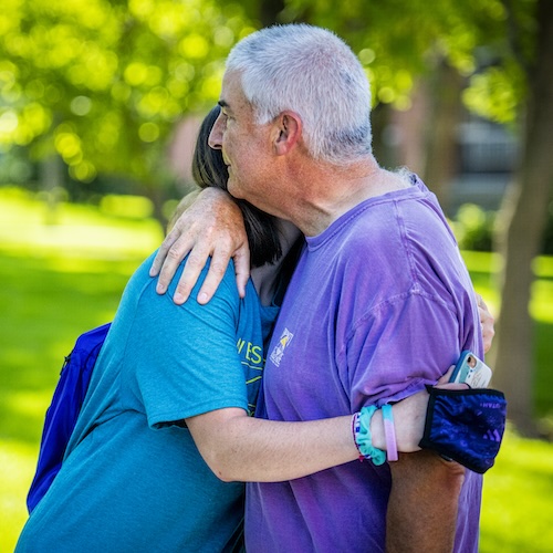 Father and daughter embracing during college move-in day, surrounded by green trees