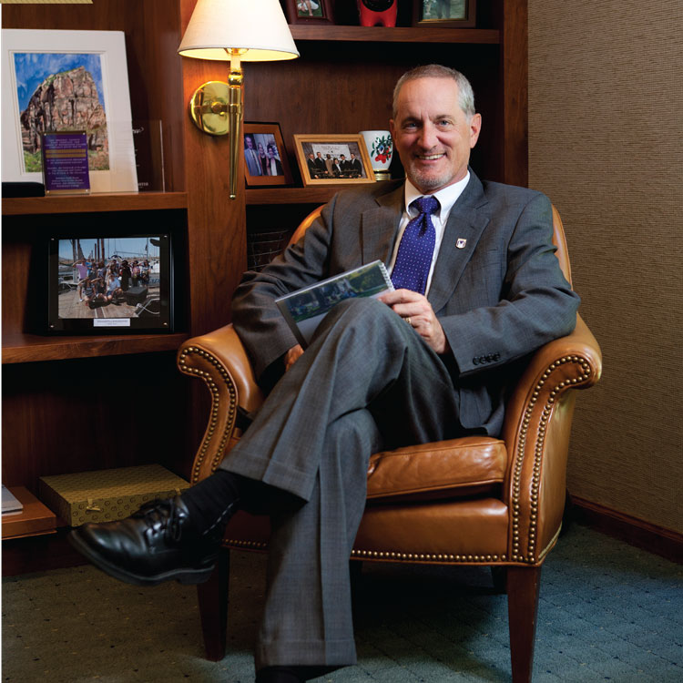 Dr Brian sitting in leather chair with book