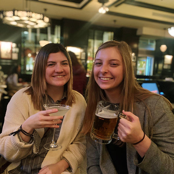 Lauren Hofstra and Cami Mondeaux clanking two beer mugs together