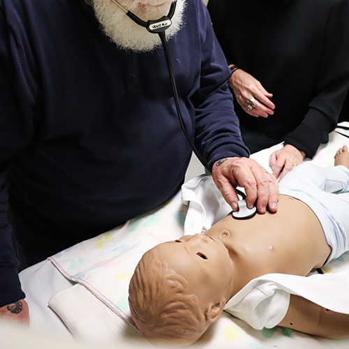 person using a stethoscope on a simulation infant