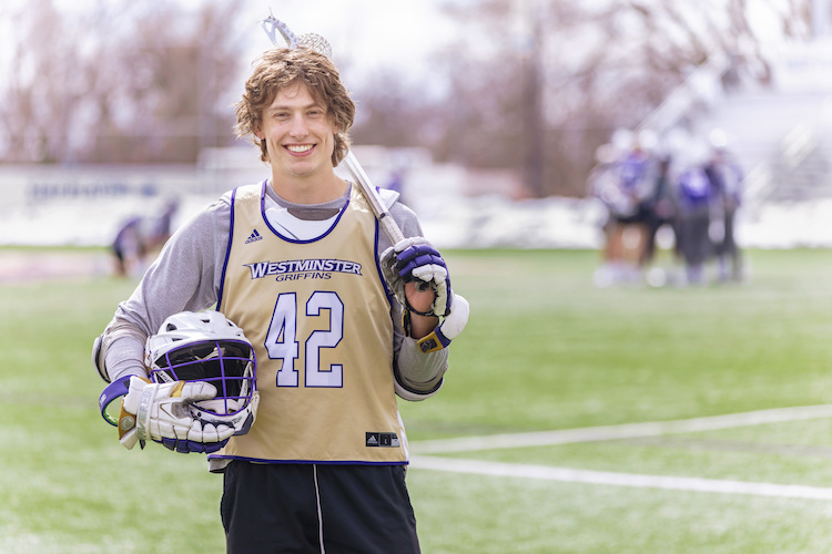 Westminster lacrosse player posing on the field with their gear