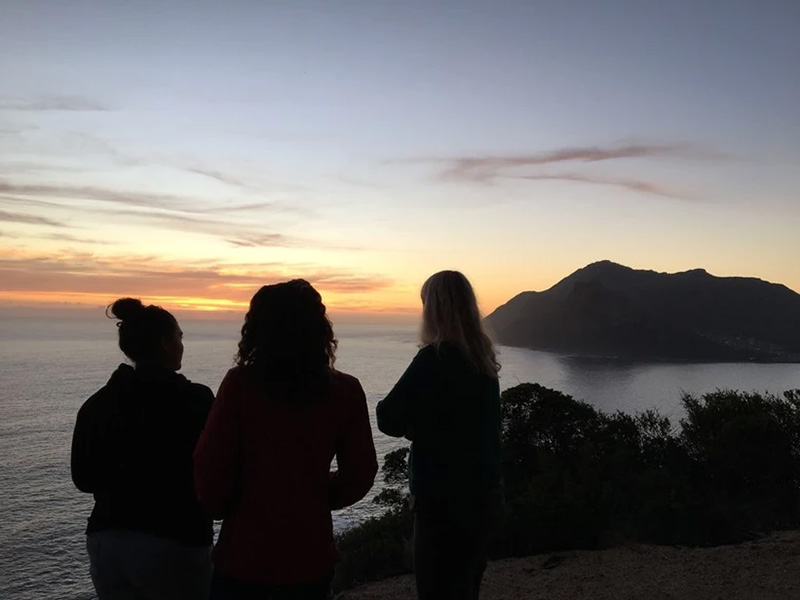 three shadowy individuals pose in front of lake and sunset